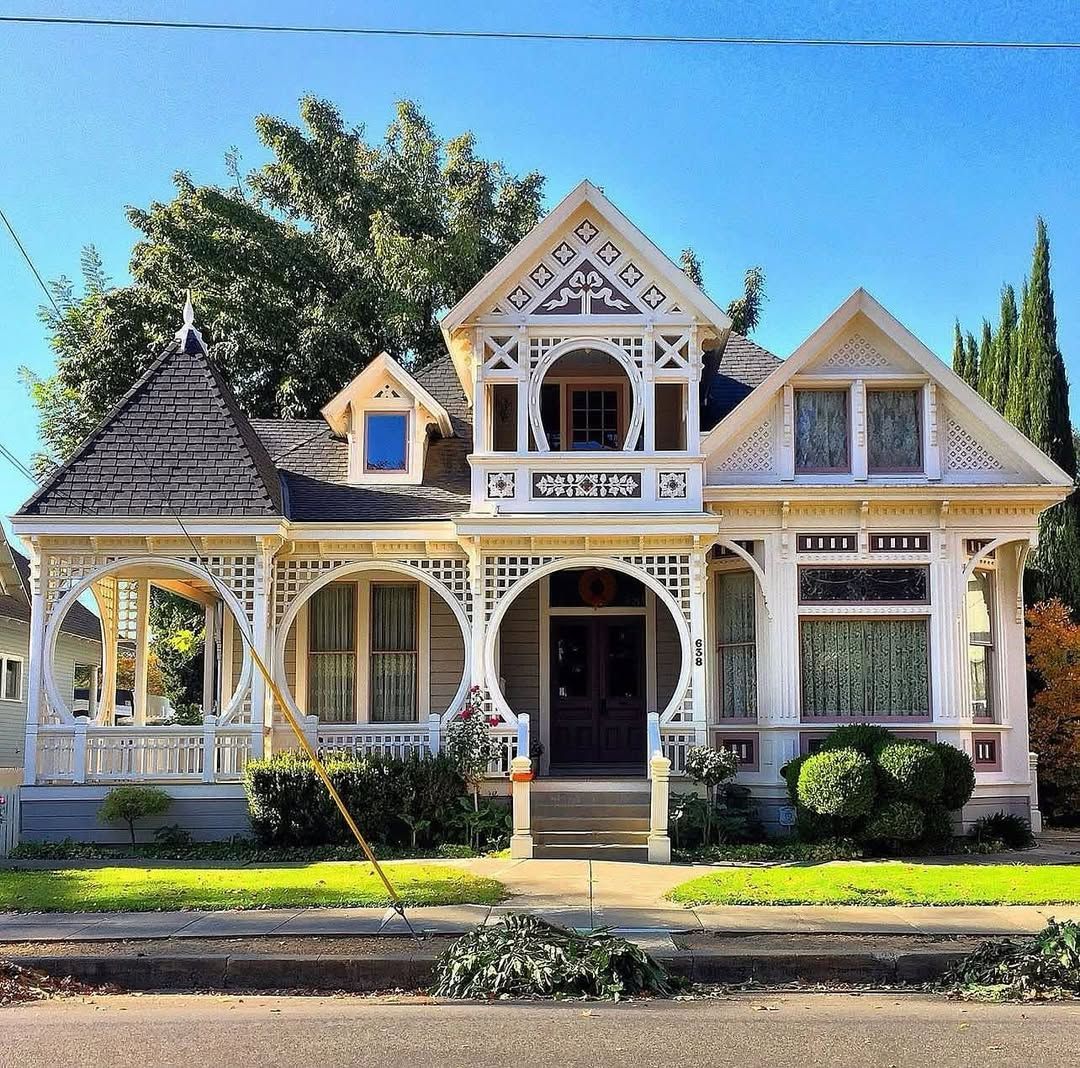 White Victorian house with ornate details, wraparound porch, and turret on a sunny day