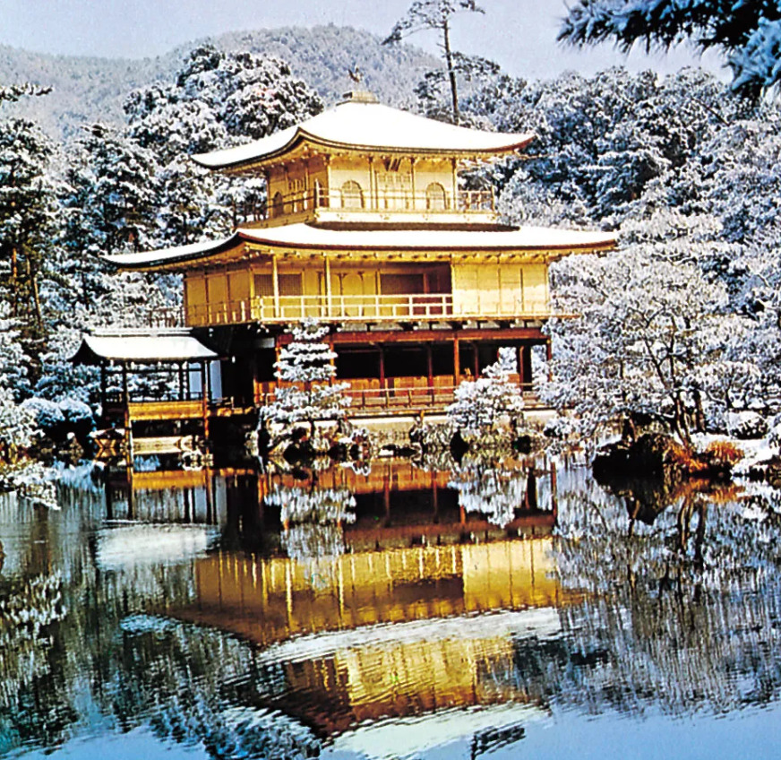Golden temple with three tiers reflecting in pond, surrounded by snow-laden trees and white winter landscape