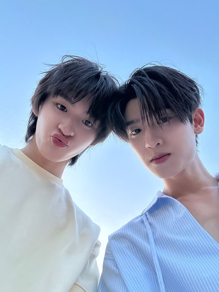 Two young Asian men posing for a selfie against a blue sky background