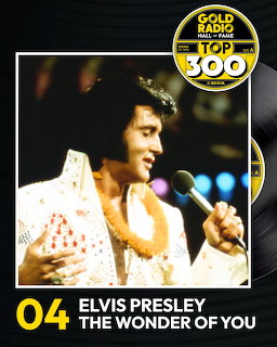 Elvis Presley singing on stage in a white jumpsuit, holding a microphone