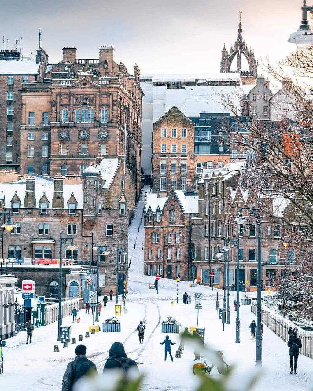Snowy winter scene in Edinburgh with historic sandstone buildings and people walking on snow-covered streets