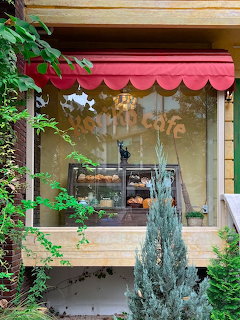 Cafe window with red awning framed by green plants and foliage