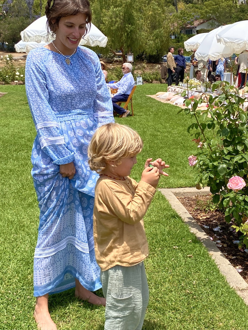 Young boy with camera standing beside woman in blue dress in rose garden