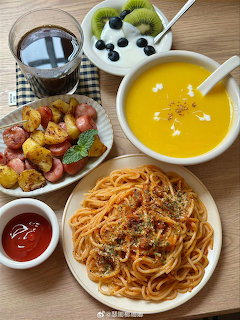 Overhead view of a meal with spaghetti, yellow soup, roasted potatoes, fruit yogurt, and cola on a table