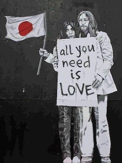 Black-and-white street art of two figures holding a love sign beside a Japanese flag