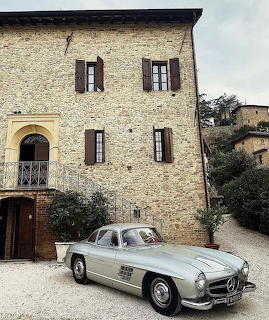 Silver Mercedes 300SL parked beside a rustic stone house