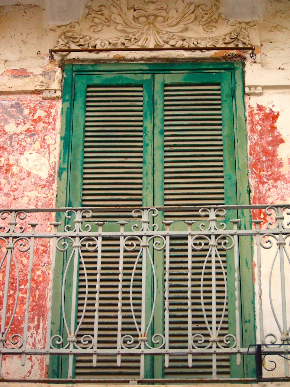 Weathered green shuttered balcony window on a faded red and cream wall