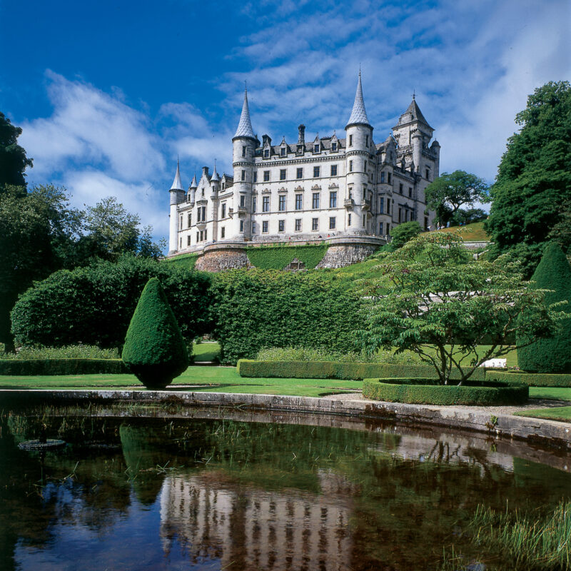 Dunrobin Castle with white spires and turets seen from formal gardens with topiary and a pond