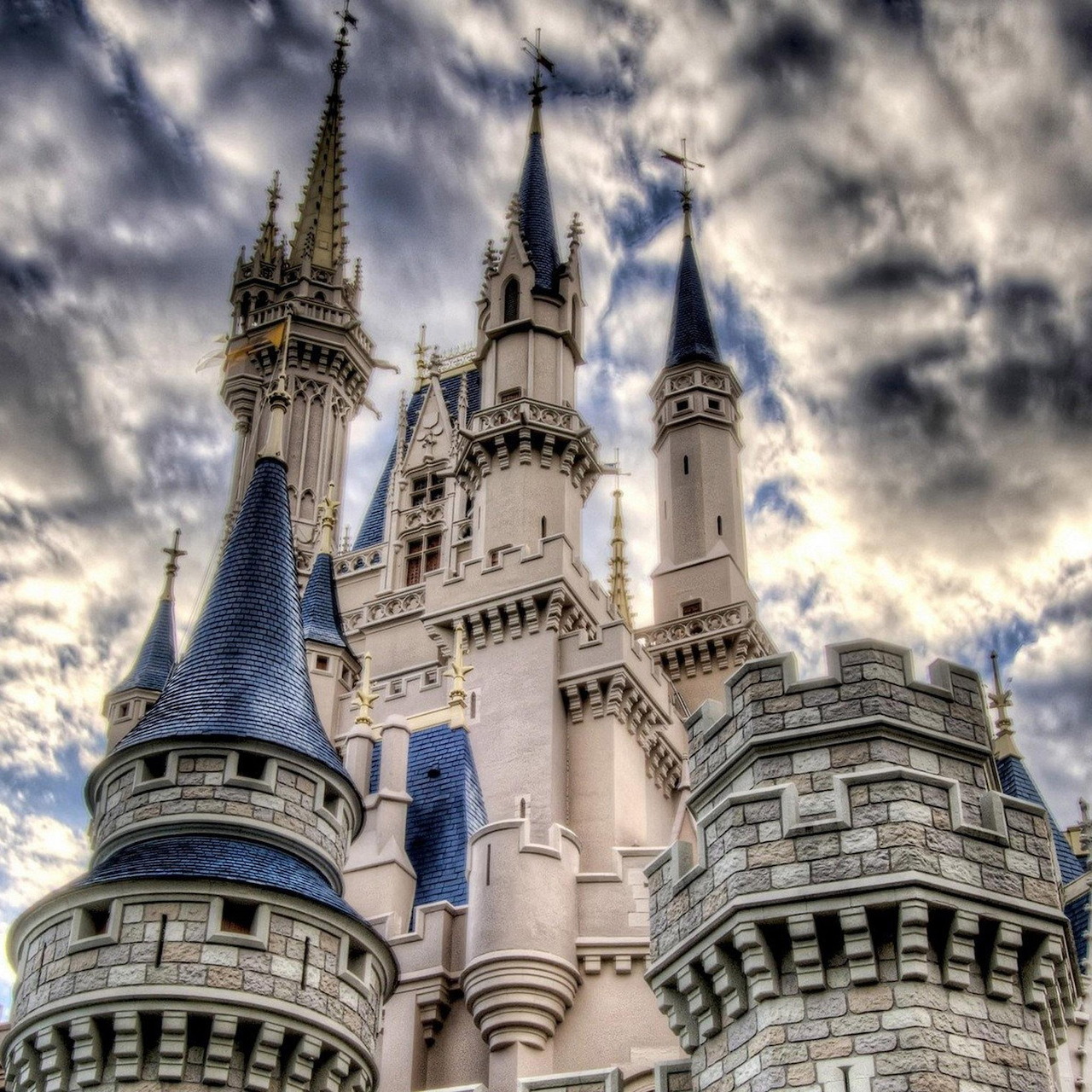 White castle with blue conical spires reaching toward dramatic cloudy sky