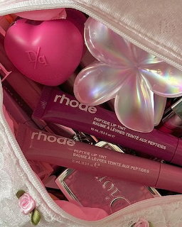 Pink makeup bag filled with Rhode lip tint products, a heart-shaped beauty item, and a holographic flower
