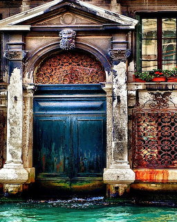 Ornate weathered doorway with blue doors and white columns opening onto Venice canal water