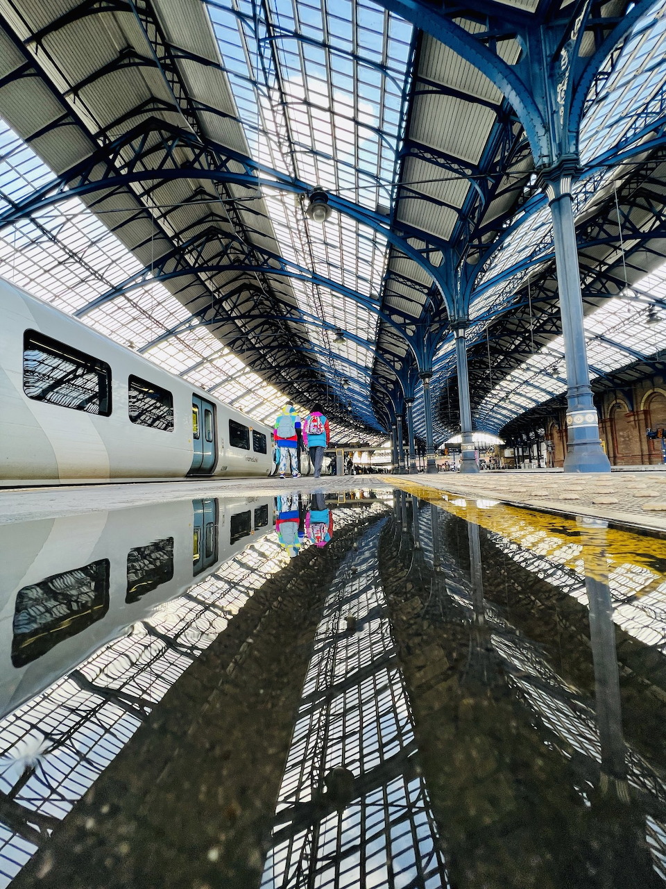 Symmetrical view of Brighton railway station interior with ornate glass roof and iron beams reflected below
