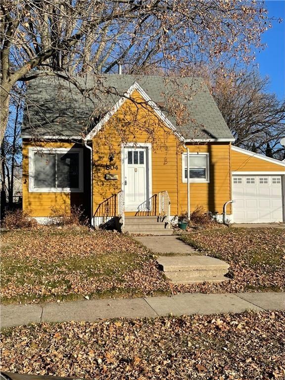 Yellow house with white door and garage, bare trees and fallen leaves in autumn