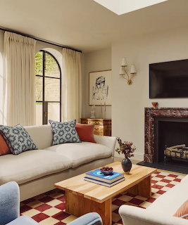 Stylish living room with cream sofa, marble fireplace, arched window, and red-white checkerboard rug