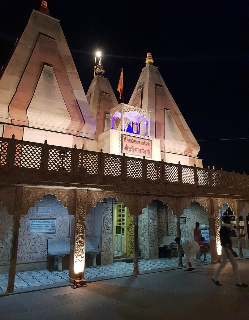 White Hindu temple with tall spires lit at night, showing arched entrance and visitors