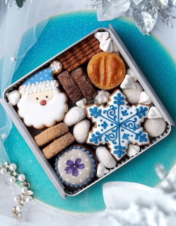 Christmas cookies in gift box with snowman, house, and snowflake designs on turquoise plate with winter decor