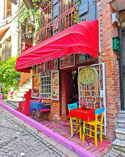 Colorful cafe exterior with pink awning, rainbow chairs and tables on cobblestone street