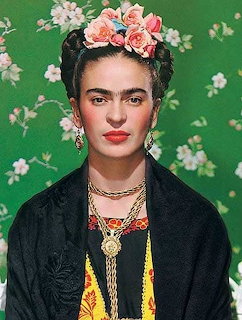 Portrait of Frida Kahlo with pink flowers in her hair, gold jewelry, and black jacket against green background