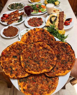 Plate of lahmacun flatbreads on a table with salads, grilled meat, and side dishes