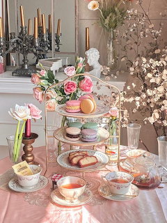 Vintage tea table with floral china, pastries, candles, and a tiered dessert stand