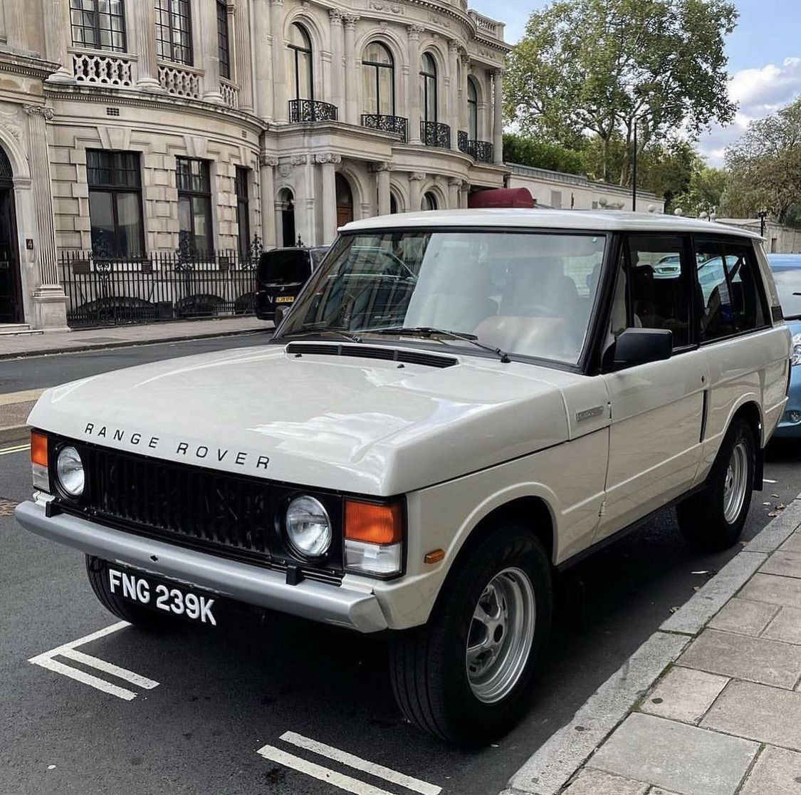 White classic Range Rover SUV parked on urban street with historic buildings behind