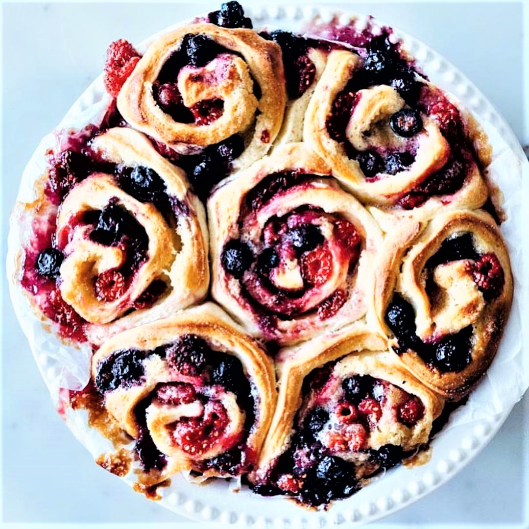Top view of berry-filled spiral pastry buns on white plate with powdered sugar