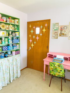 Midcentury-style room corner with green bookshelf, wooden door with star decals, pink desk and floral chair