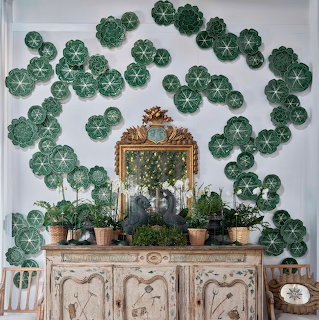 Vintage console table with ornate mirror, plants in terracotta pots, and green decorative plates on white wall