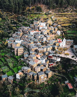 Aerial photograph of a compact hillside village with traditional buildings nestled among green terraced slopes and trees
