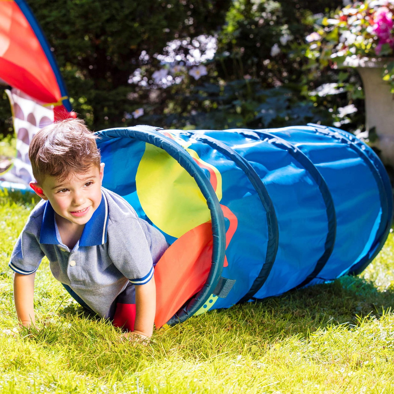 Young boy crawling through a colorful play tunnel on grass outdoors