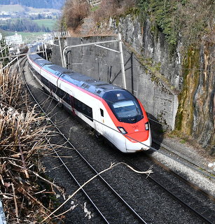 Modern red and white high-speed train on curved mountain railway track with stone walls