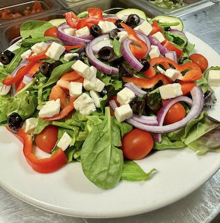 Plate of fresh salad with lettuce, tomatoes, cucumbers, red onion, olives, peppers, and feta cheese