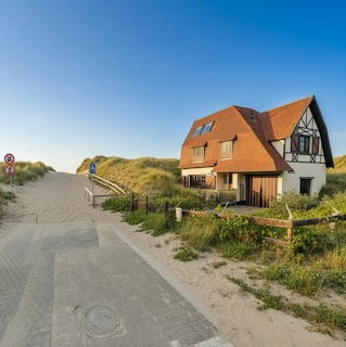 Coastal house beside a sandy path and grassy dunes under a blue sky