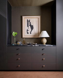 Dark gray dressing room cabinet with marble top, table lamp, and framed abstract art on wall