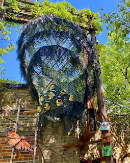 Tall mosaic sculpture of a face with geometric patterns in blue and green tiles outdoors