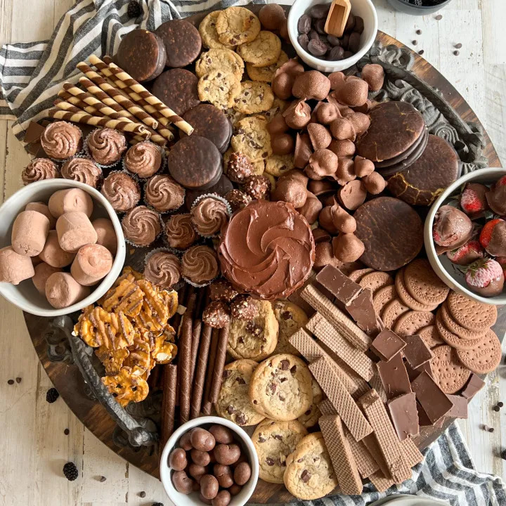 Overhead view of a circular wooden board with assorted chocolate desserts, cookies, and fresh berries