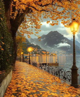 Autumn lakeside walkway covered in golden leaves with lit street lamps and mountains in background