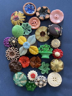 Collage of colorful decorative buttons with floral and geometric patterns arranged on blue fabric background