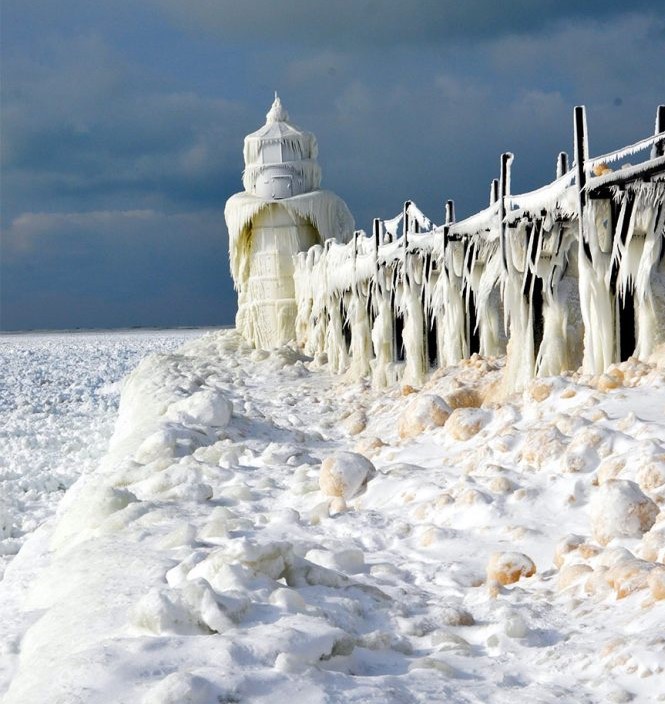 Ice-covered lighthouse and pier with icicles along a frozen snowy shoreline