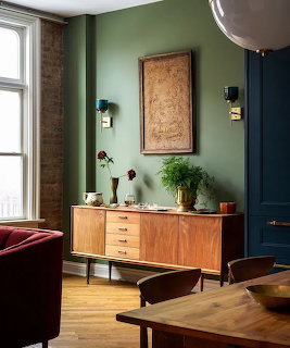Mid-century wood credenza with drawers against a green wall decorated with plants and framed artwork