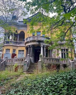 Abandoned yellow manor with stone balconies and columns covered in ivy and overgrown vegetation