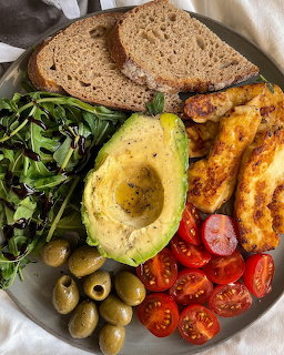 Plate of avocado, bread, olives, cherry tomatoes, greens, and cooked egg