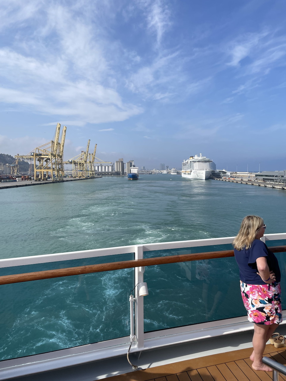 Woman on a ship deck looking over Barcelona harbor with port cranes and a cruise ship