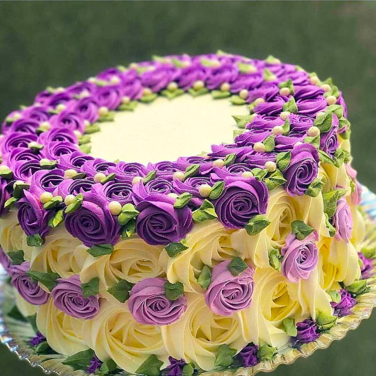 Round cake decorated with purple, yellow, and pink buttercream roses in concentric rings