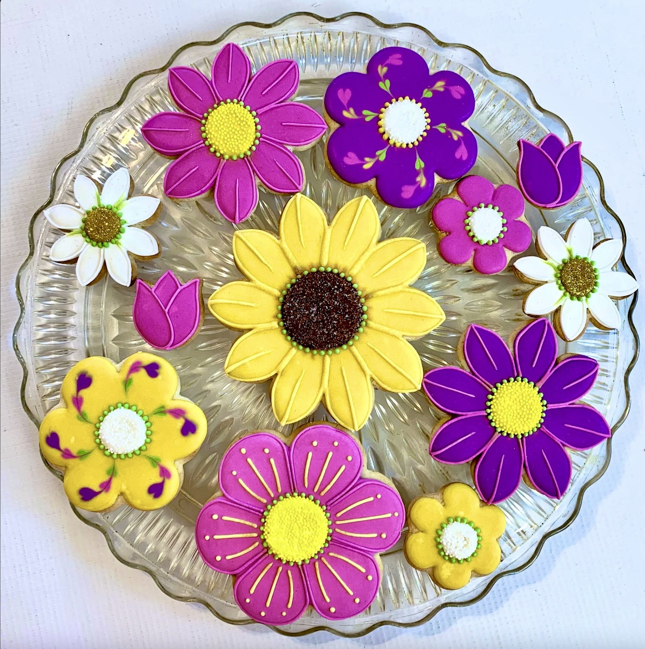 Colorful flower-shaped iced cookies arranged on a glass plate