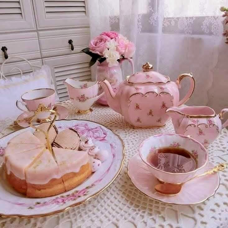 Pink teapot, teacup, and frosted cake on a lace table with flowers