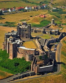 Aerial view of Bamburgh Castle with stone walls, green grounds, and surrounding farmland