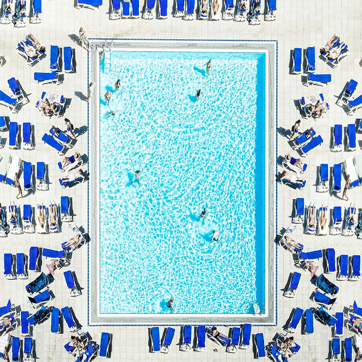 Overhead view of rectangular swimming pool with blue lounge chairs and umbrellas on white deck
