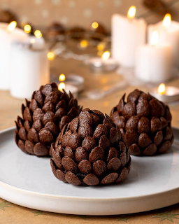 Three chocolate pinecone-shaped desserts on a plate with candles behind