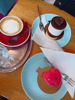 Cappuccino with latte art and two desserts on a cafe table
